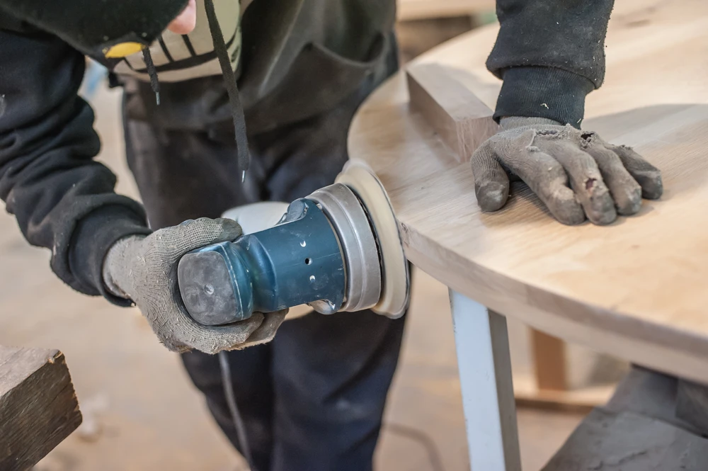 Atelier de menuiserie intérieur avec artisan utilisant une ponceuse électrique sur meuble en bois brut