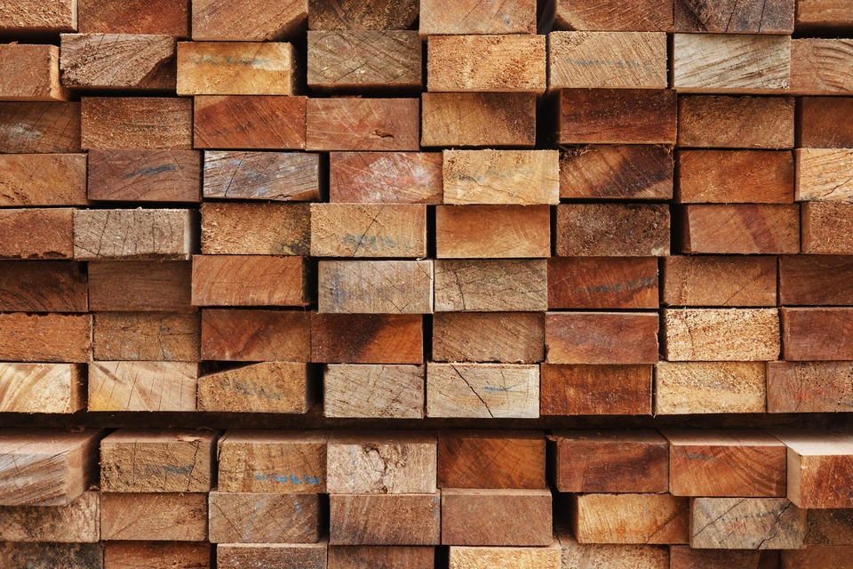 Empilement de planches de bois sciées stockées en extérieur, présentant différentes essences et nuances naturelles allant du brun clair au rougeâtre