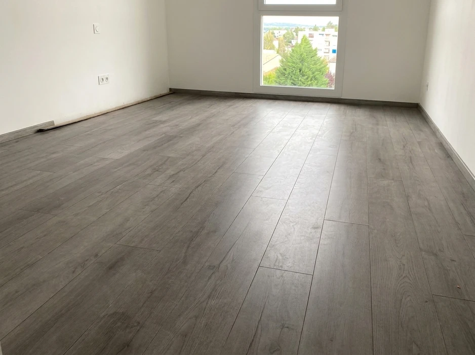 Pièce vide lumineuse avec sol en parquet stratifié gris taupe, lames larges posées en quinconce