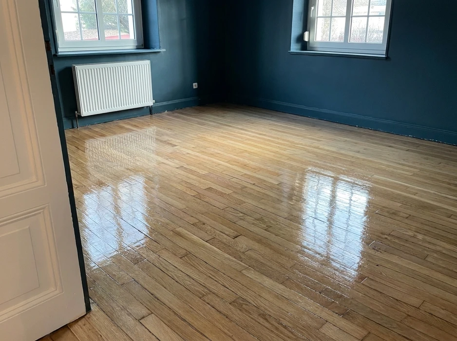 Pièce vide aux murs bleu pétrole, parquet en lames de chêne massif récemment vitrifié, finition brillante haute luisance encore fraîche