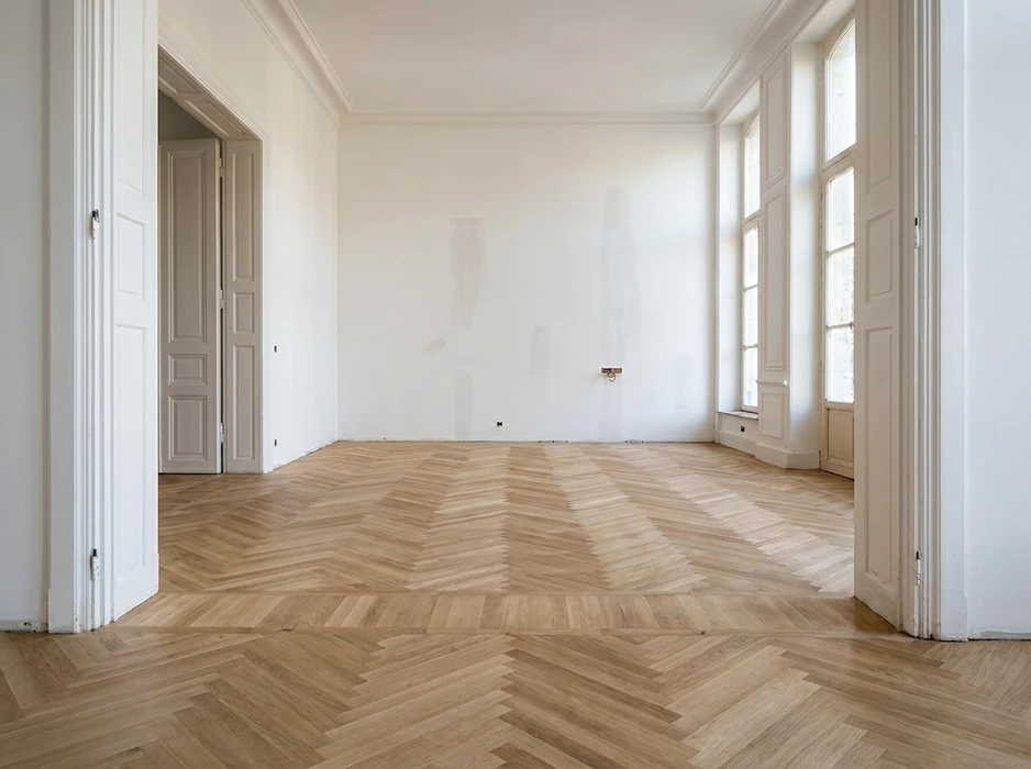 Pièce vide en cours de rénovation, parquet point de Hongrie en chêne clair non traité, murs blancs avec traces d'humidité, moulures corniche plafond, double porte à panneaux style haussmannien, grandes fenêtres à petits bois, prise électrique apparente en attente
