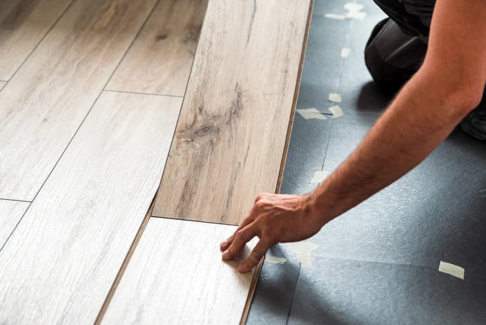 Homme agenouillé installant du parquet stratifié dans un intérieur résidentiel, positionnant une lame de revêtement de sol avec ses mains
