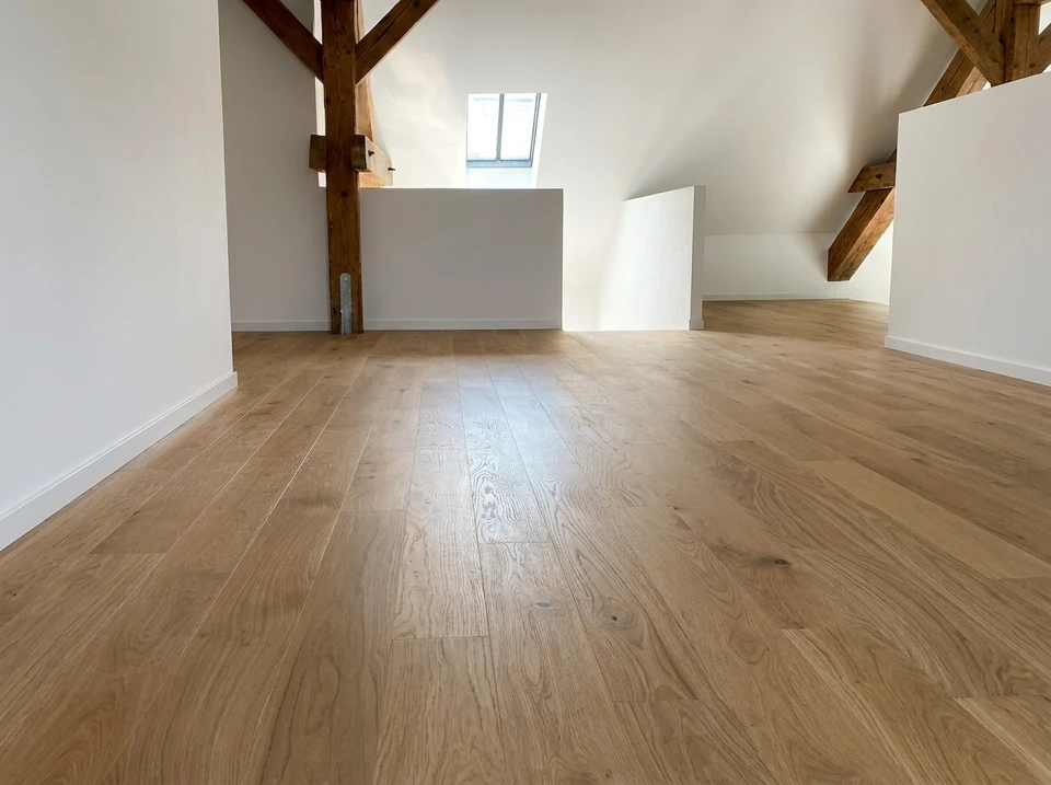 Une personne en vêtements de travail installe du parquet flottant dans un intérieur résidentiel, agenouillée sur carrelage existant