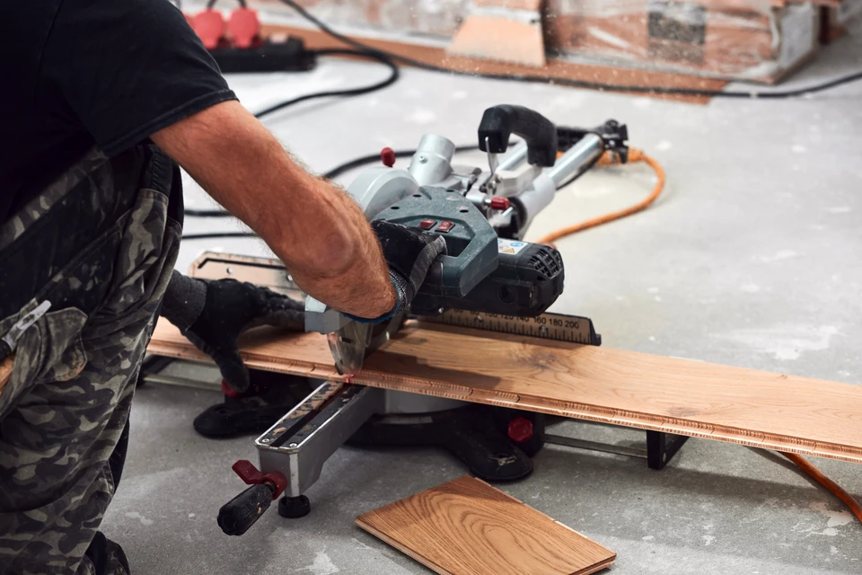 Intérieur de chantier, ouvrier en gants de protection jaunes utilisant une scie sauteuse électrique pour découper des lames de parquet stratifié