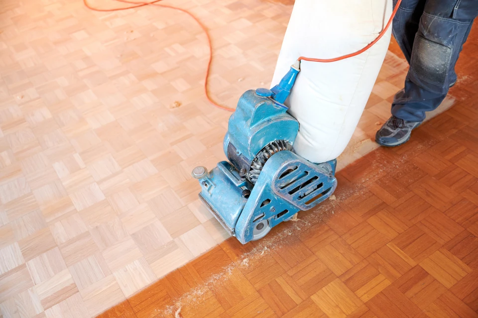 Ouvrier en combinaison blanche et masque respiratoire utilisant une ponceuse électrique murale dans un intérieur en rénovation